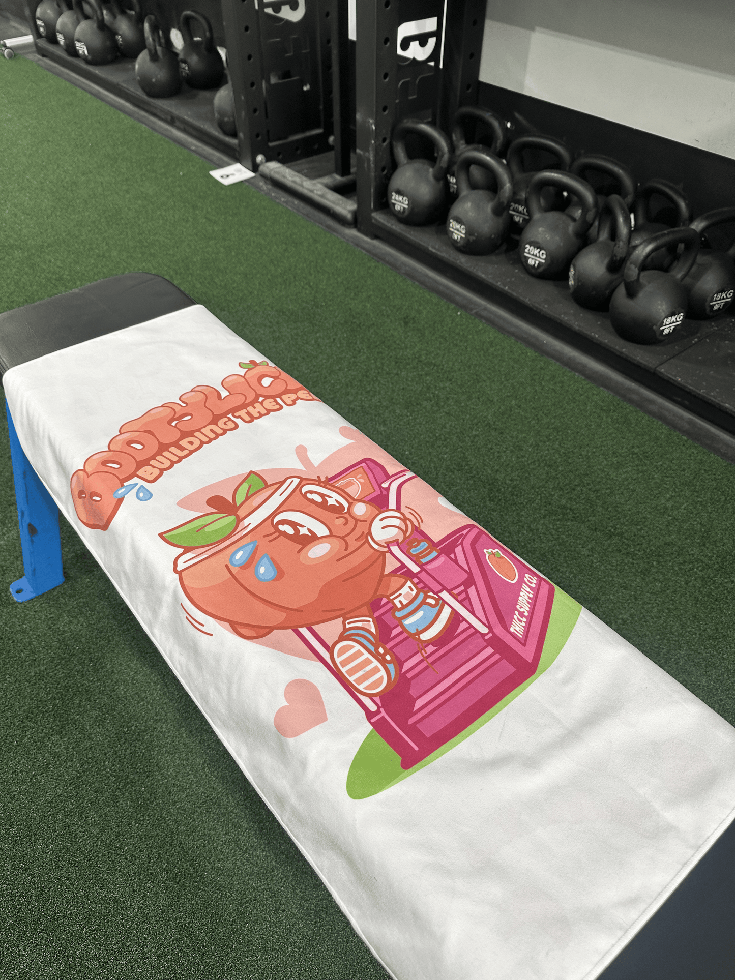 Bootylicious Gym Towel Sitting on a bench infront of Kettle Bells