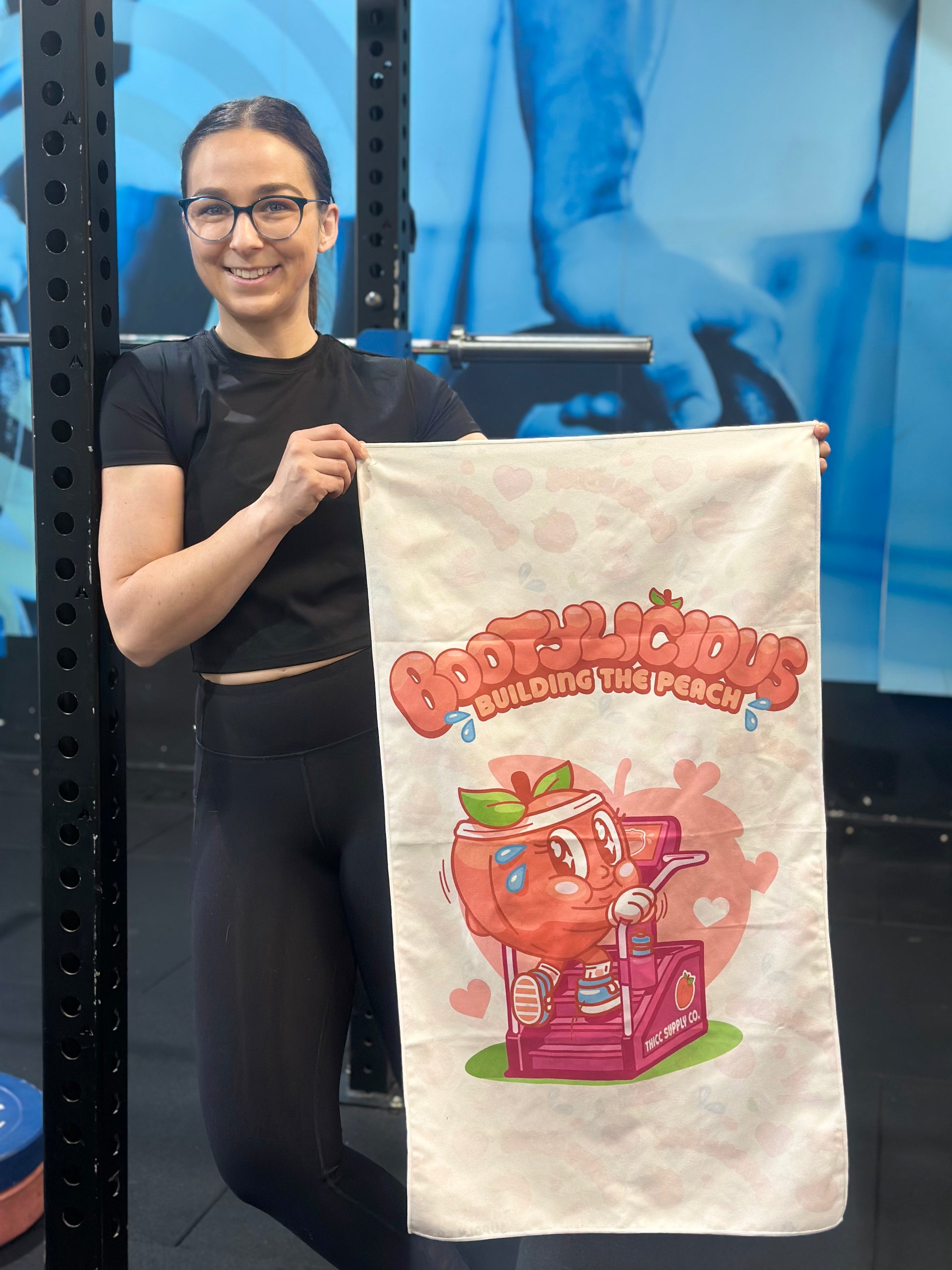 Person holding a bootylicious Gym towel - a cute cartoon peach walking on a stairmaster. 