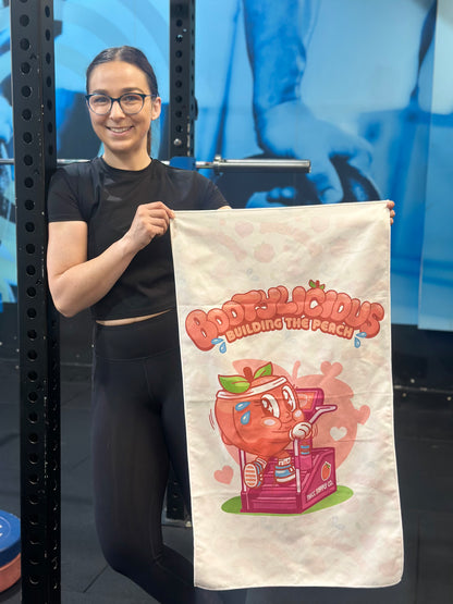 Person holding a bootylicious Gym towel - a cute cartoon peach walking on a stairmaster. 